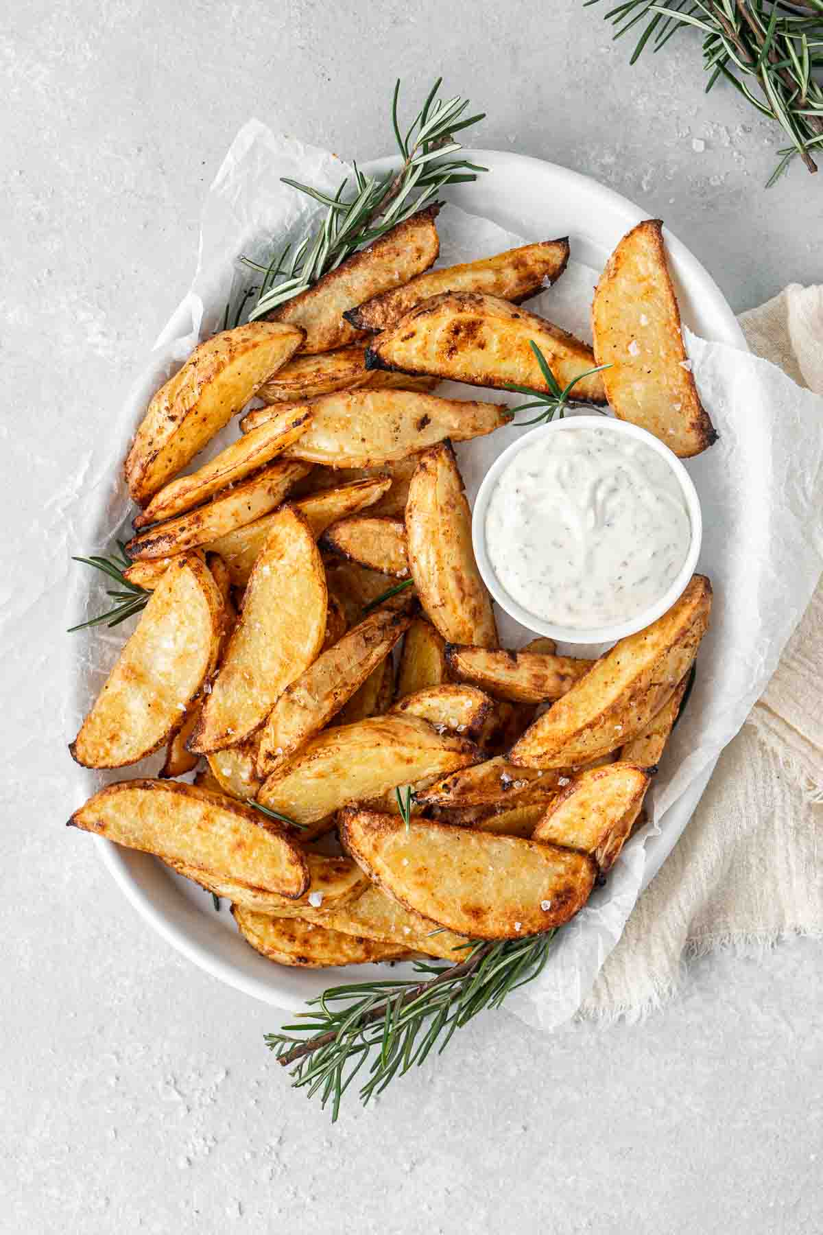 Potato wedges on a white serving platter with herb mayo and rosemary.