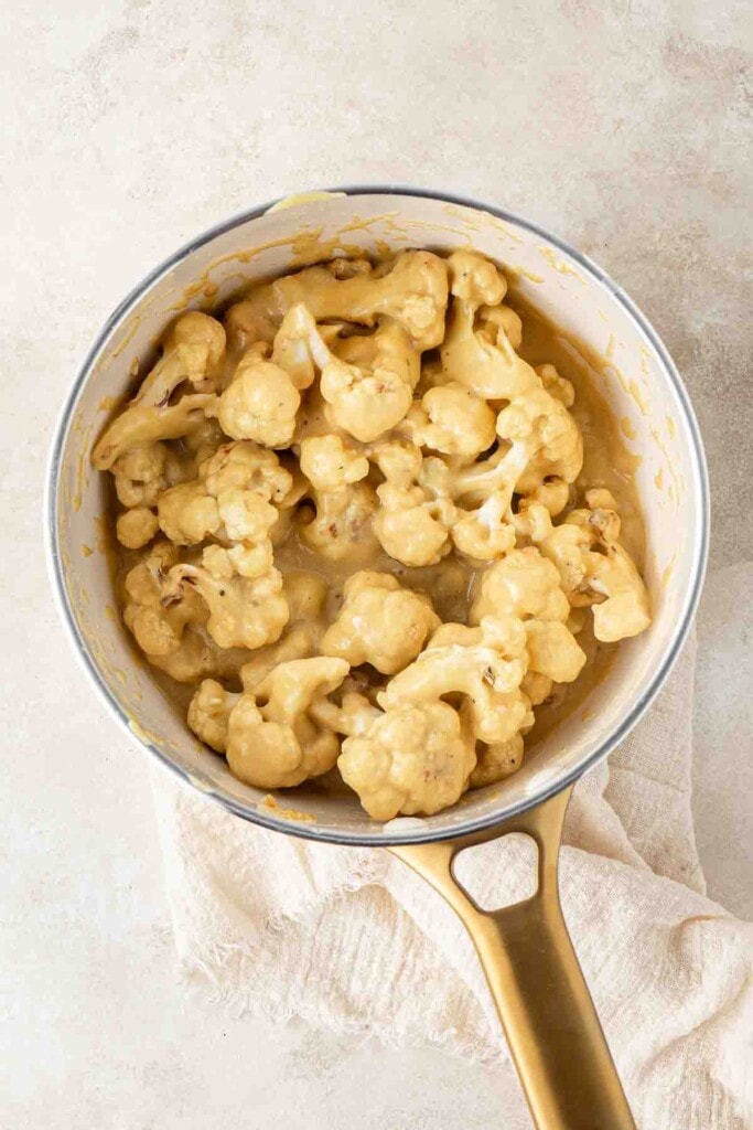 Roasted cauliflower being tossed with cheese sauce in the saucepan.