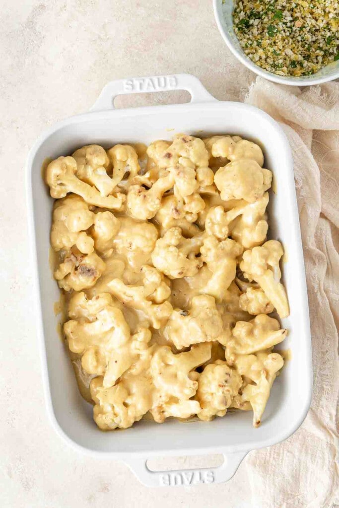 Cheese sauce mixed with cauliflower in baking dish.