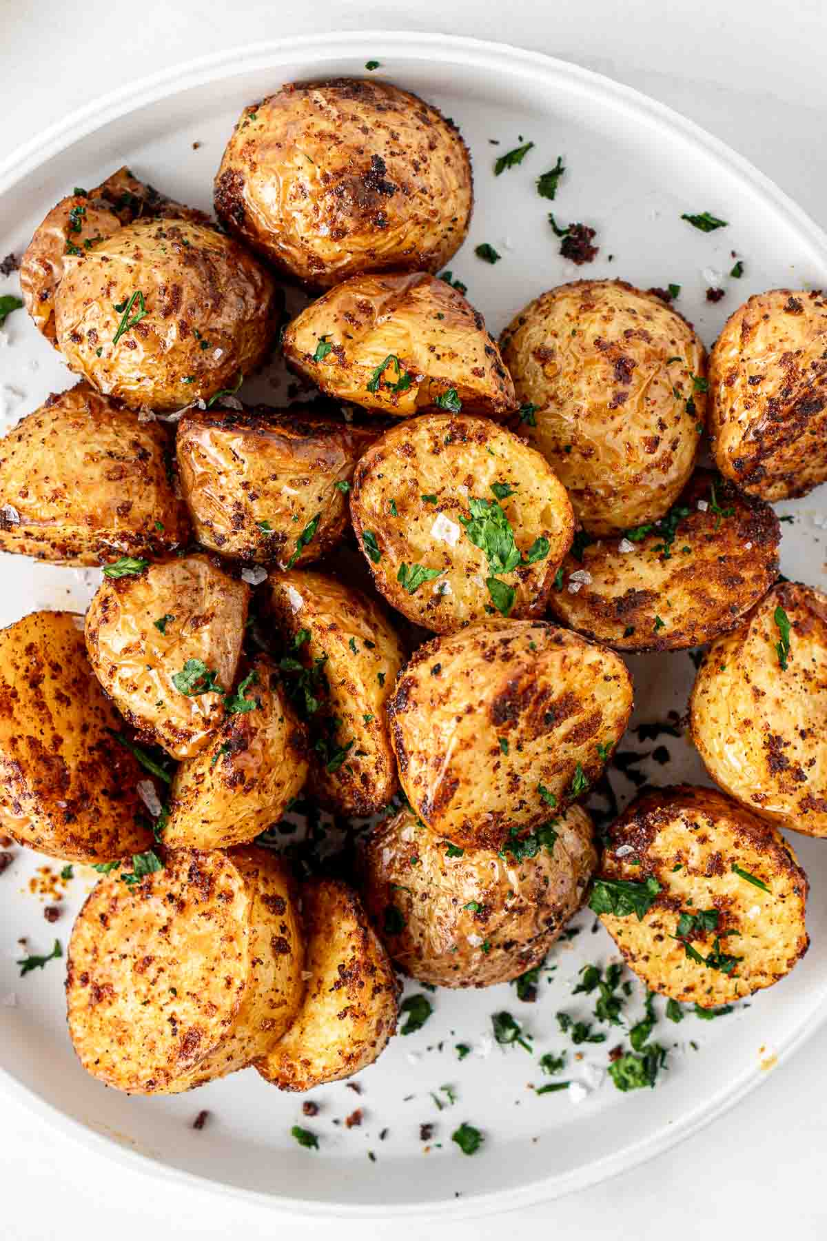 Air fryer potatoes on a white plate served with fresh parsley.