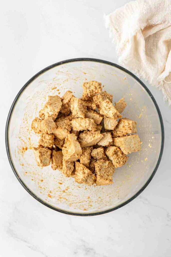Tofu pieces and sauce ingredients in a large glass mixing bowl.
