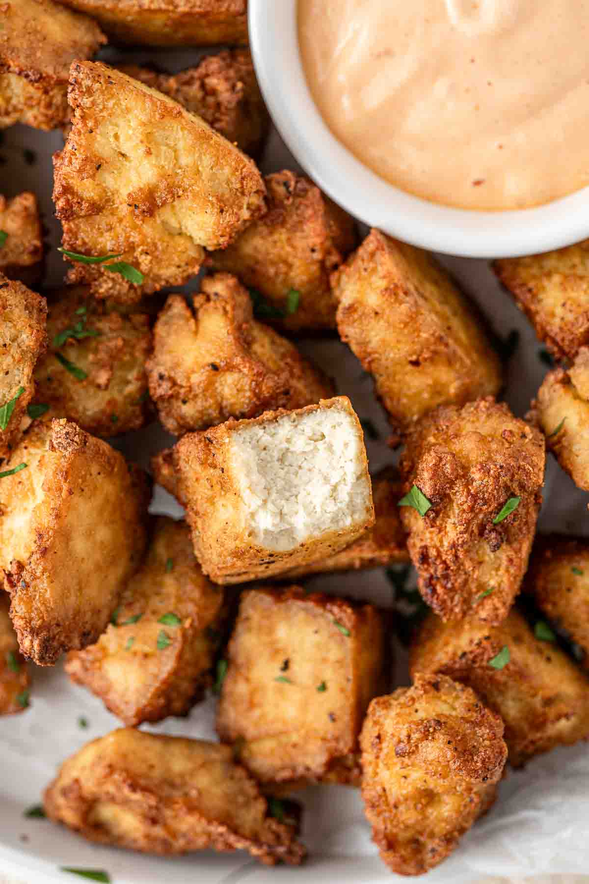 Close up of air fryer tofu nuggets, one with a bite taken revealing the inside.