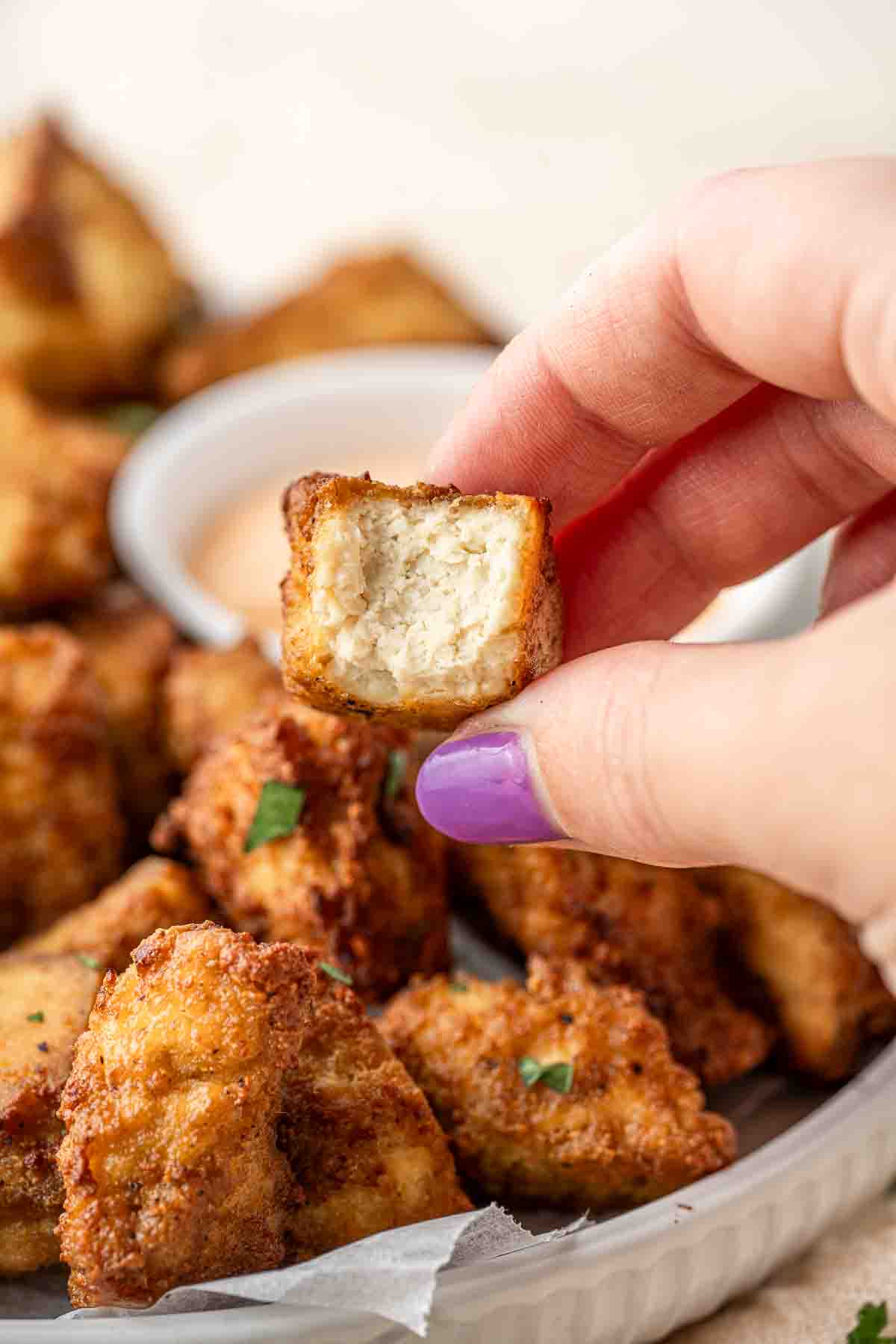 Close up of hand holding a air fried tofu nugget with a bite taken. 