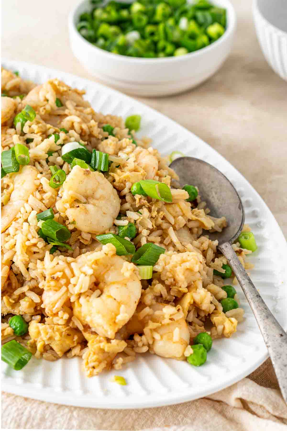 Prawn fried rice served onto a large plate with a spoon with green onions.