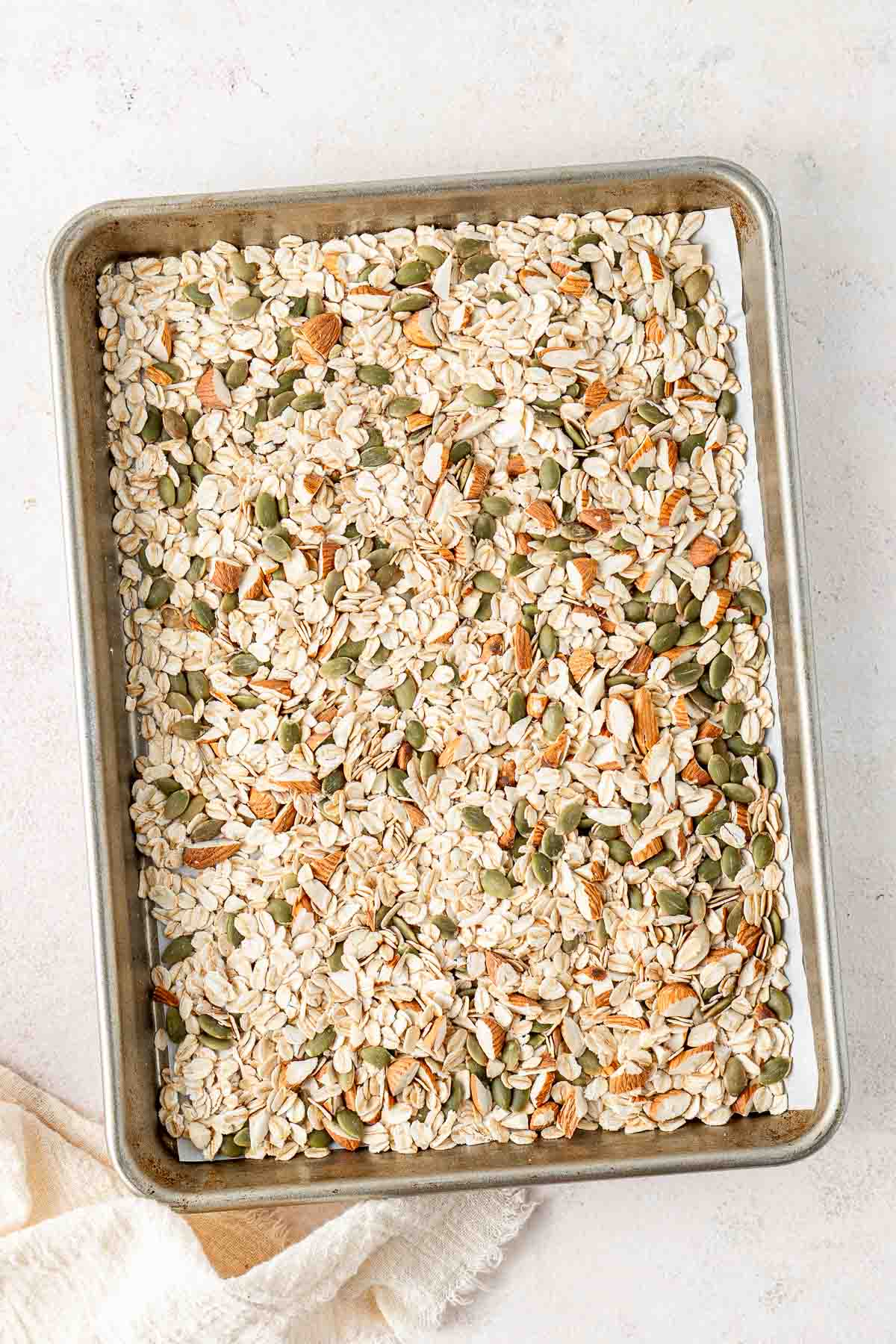 Rolled oats, chopped almonds and pepitas laid out on a baking tray to be toasted in the oven.