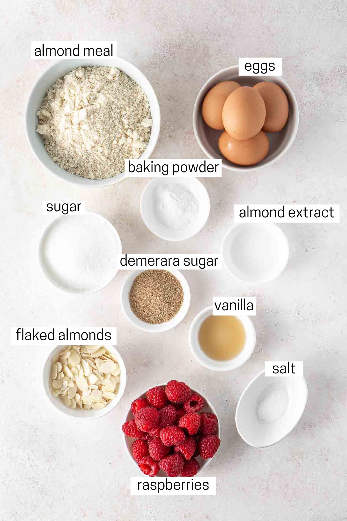 All ingredients to make gluten and dairy free almond and raspberry cake laid out in small bowls.