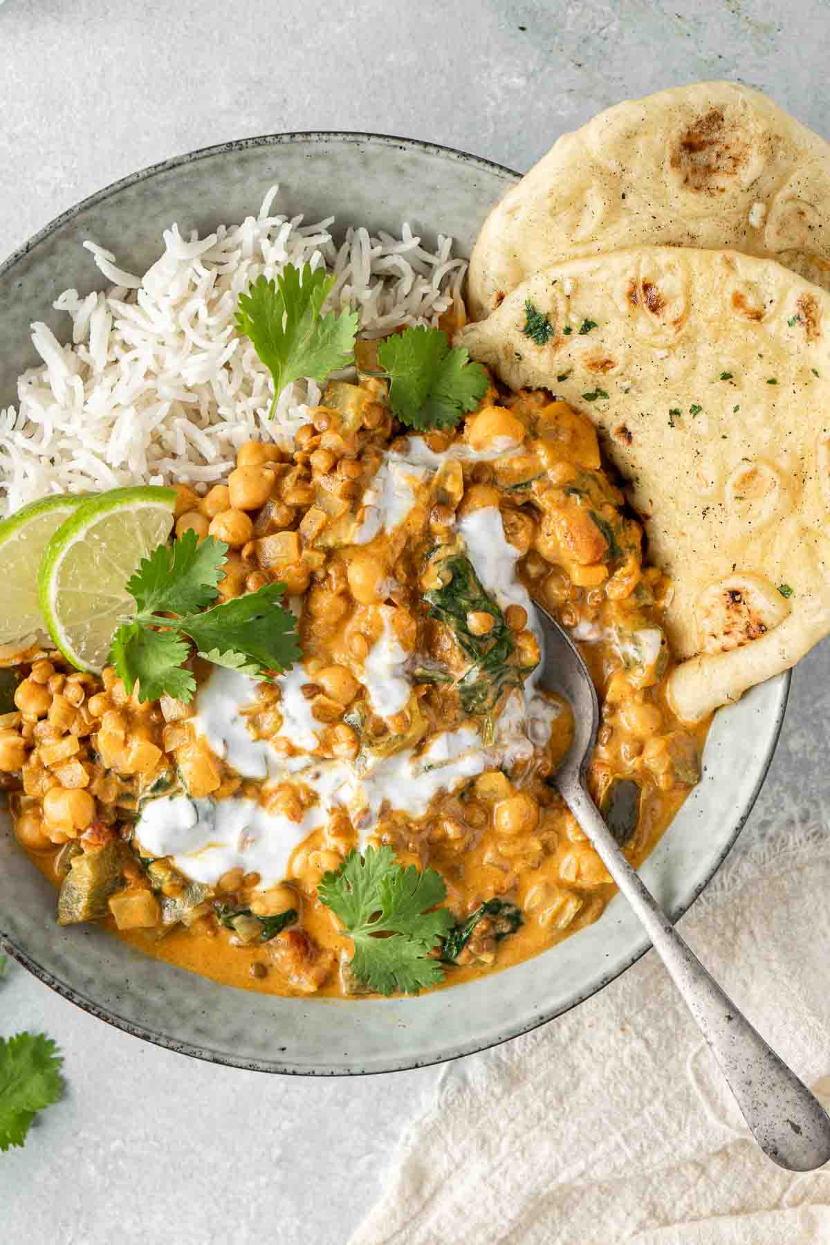 Close up of chickpea and lentil curry in a bowl over rice with naan and a spoon.