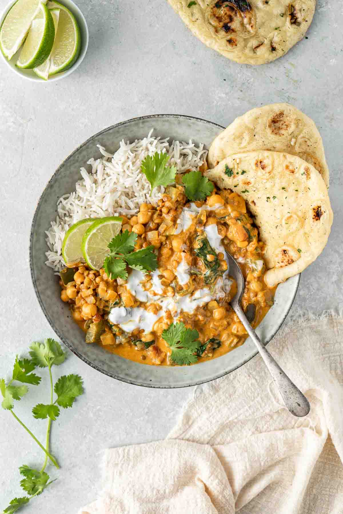 Chickpea curry in a bowl with rice, naan and cilantro.