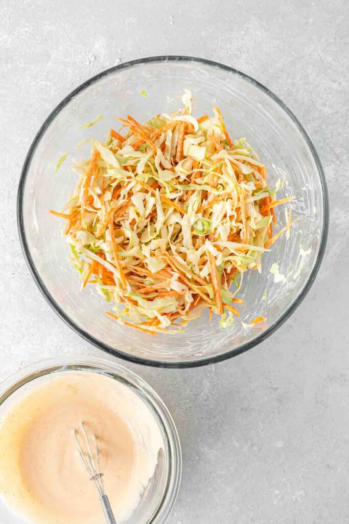 The slaw in a bowl with the prepared dressing in another bowl.