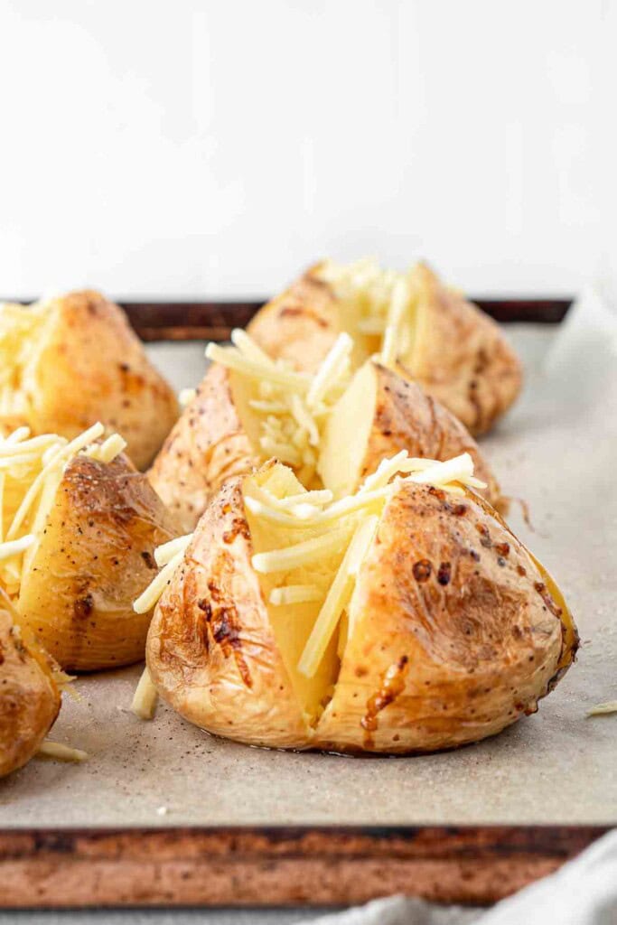 Cheese added to roasted potatoes that have been cut on a baking tray.