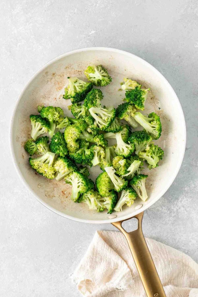 Broccoli cooking in a large frying pan.