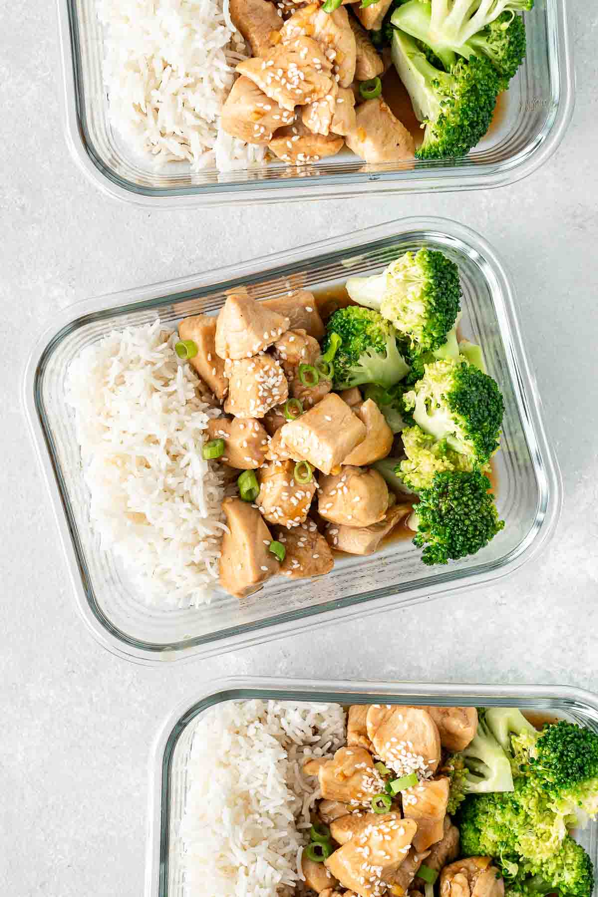 Close up of teriyaki chicken, broccoli and rice in meal prep containers with spring onion and sesame seeds. 