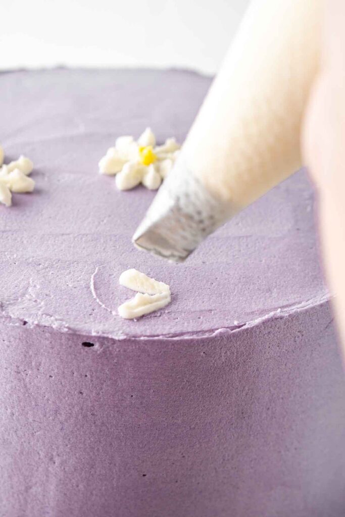 Piping daisies onto a purple cake.
