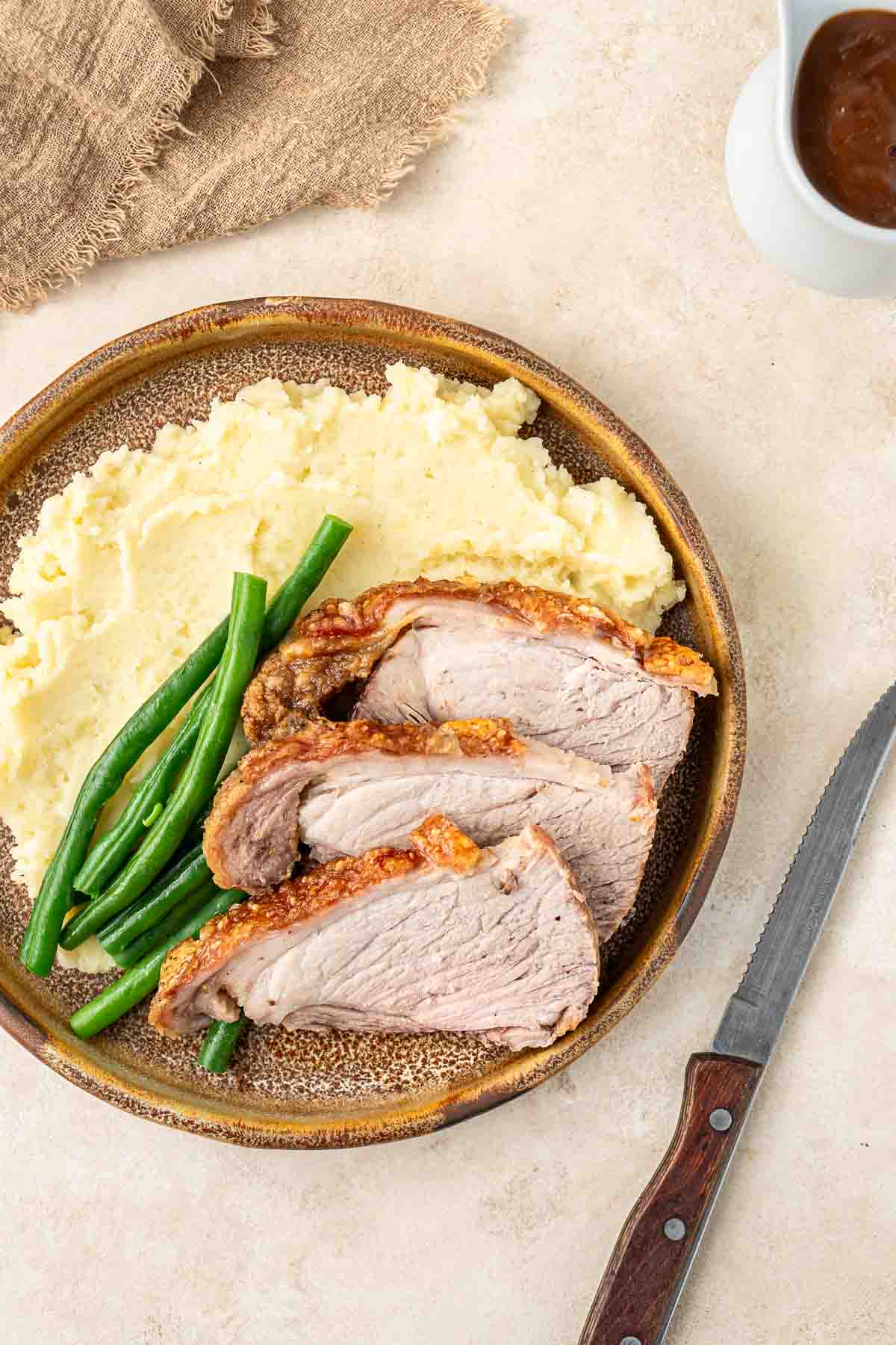 Roast pork slices and crackling over mashed potatoes and green beans.
