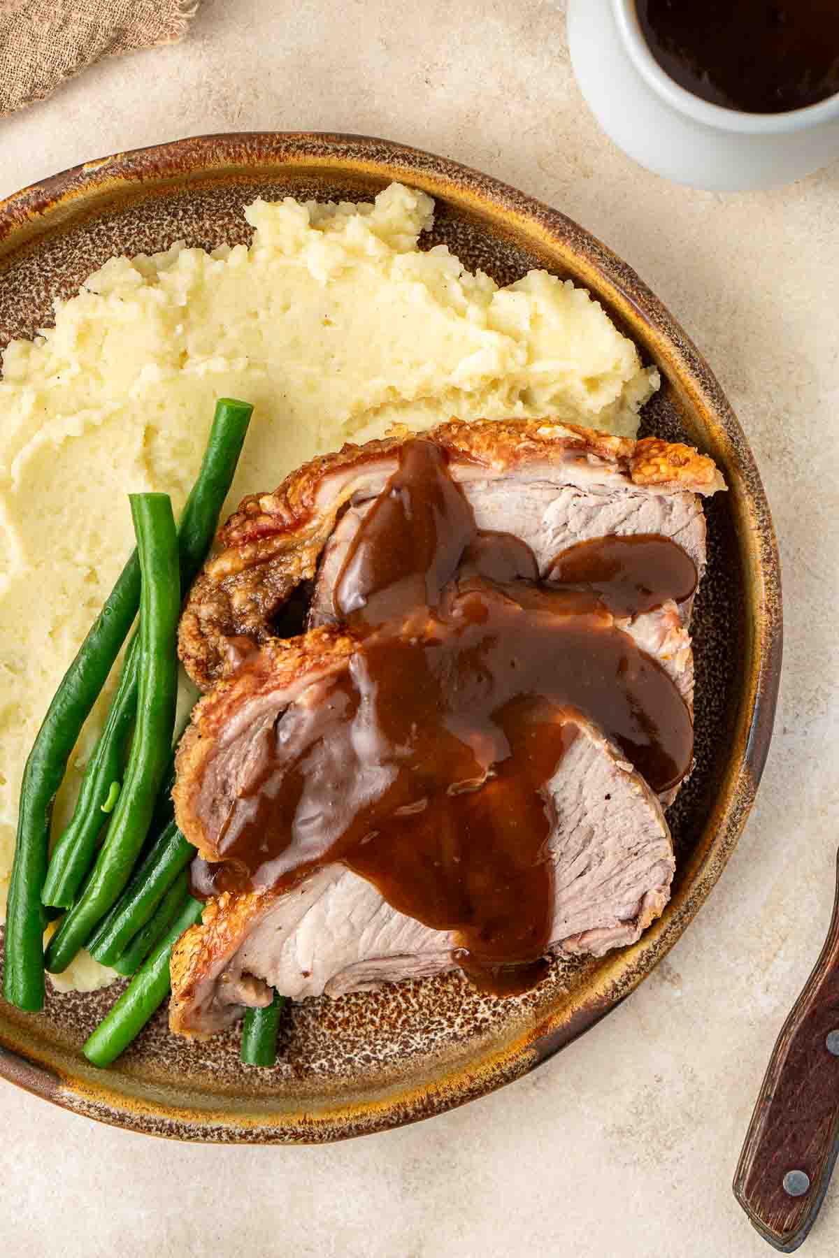 Close up of roast pork slices with gravy over mashed potatoes and green beans.