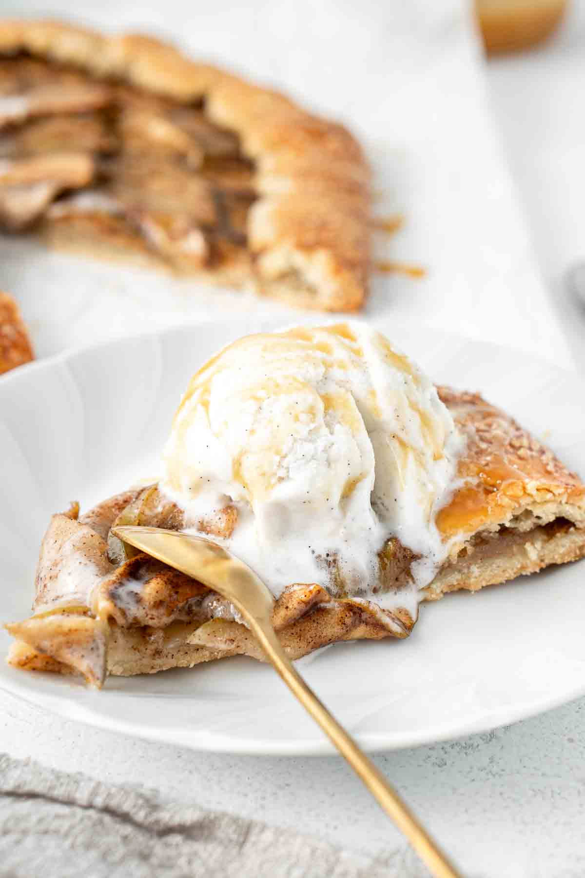 A slice of caramel apple galette with ice cream and a spoon taking a bite.
