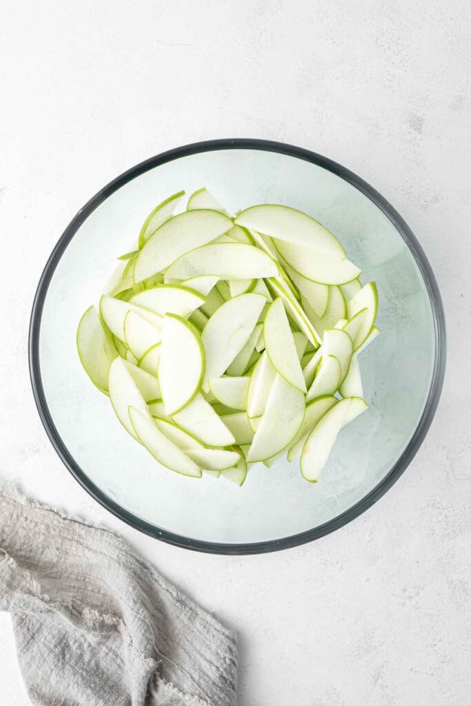 Sliced green apples in a glass mixing bowl.