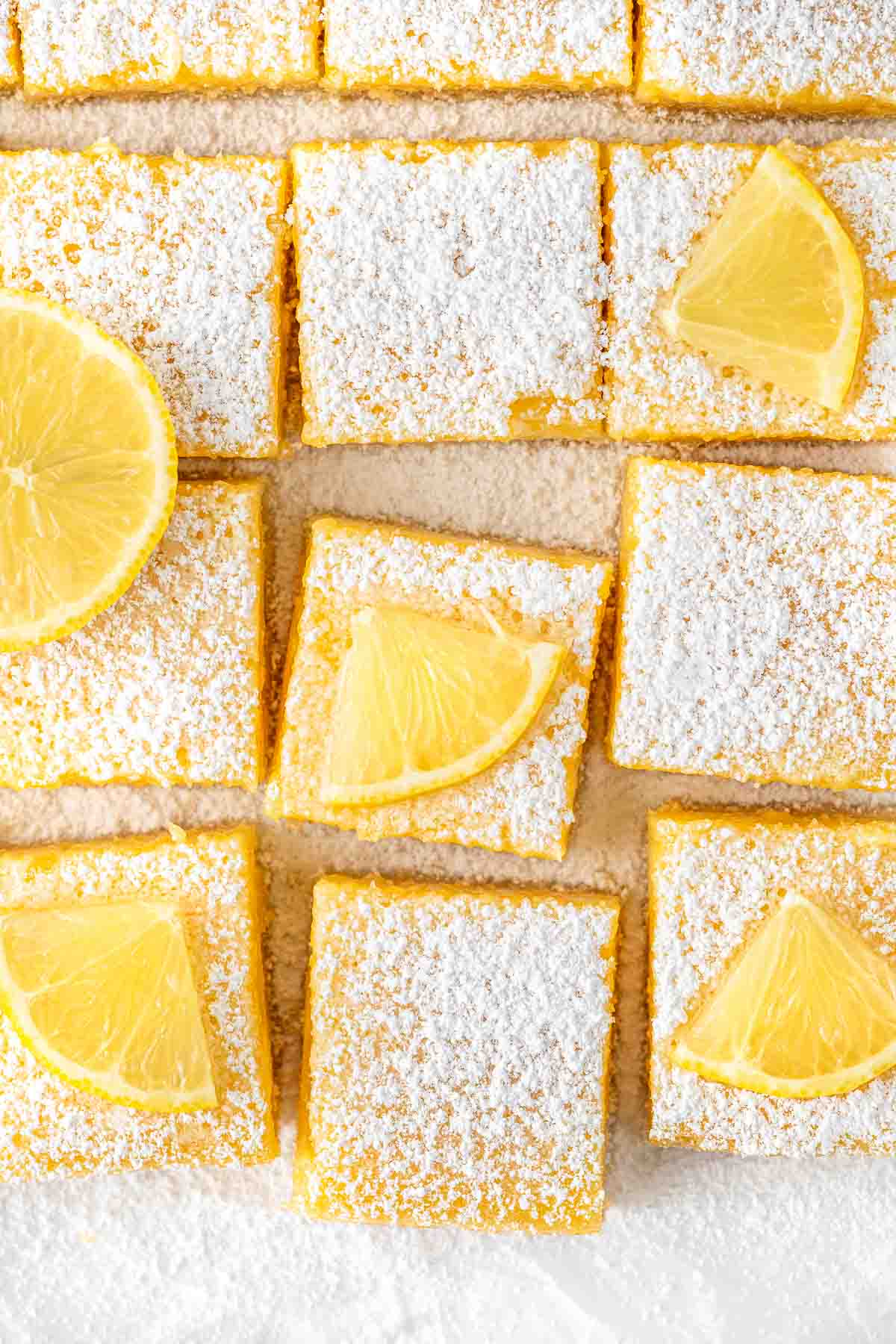 Dairy free lemon bars cut into squares with icing sugar and lemon slices.
