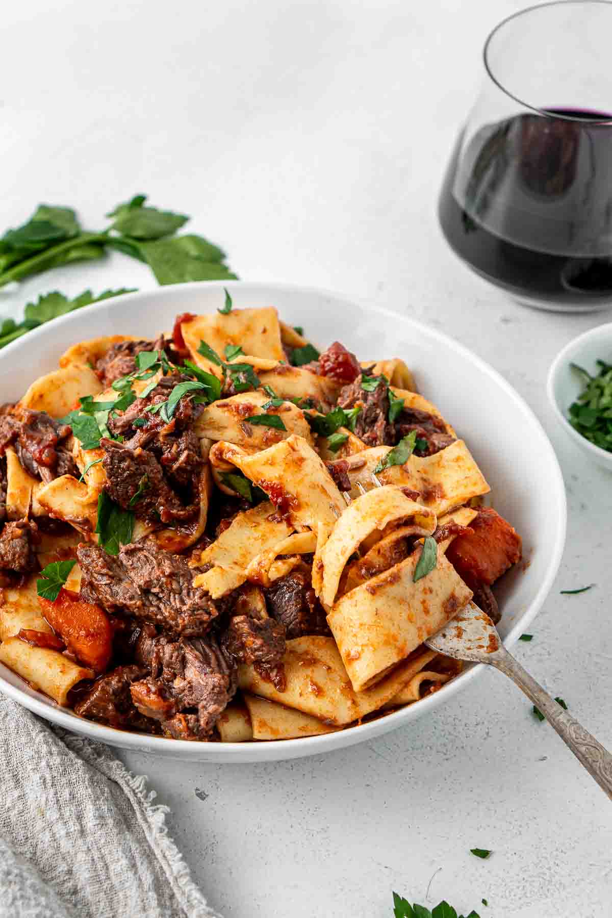 Close up of frok taking a bite of a bowl of beef ragu with pappardelle. 