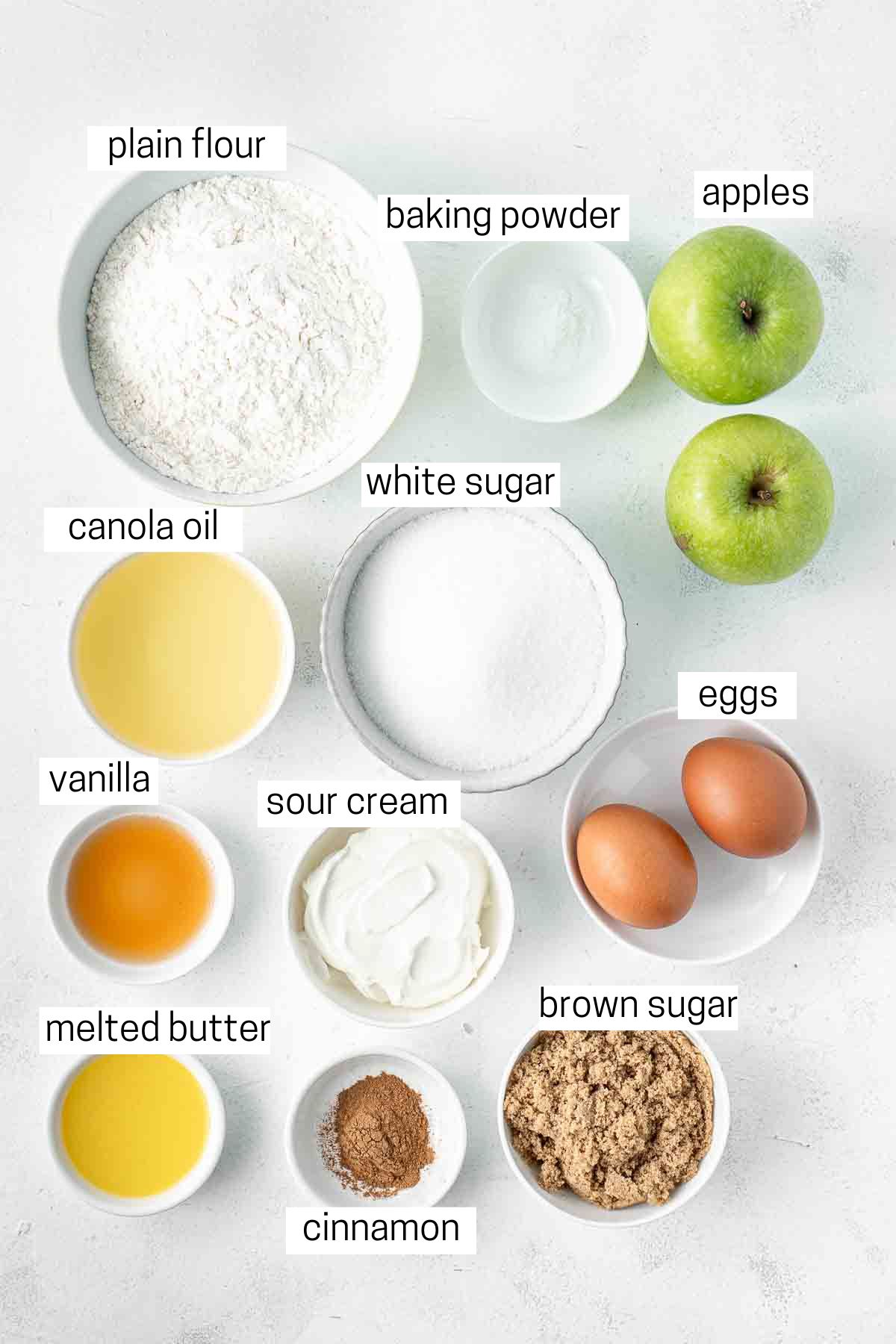 All ingredients needed to make cinnamon apple cake laid out in small bowls.