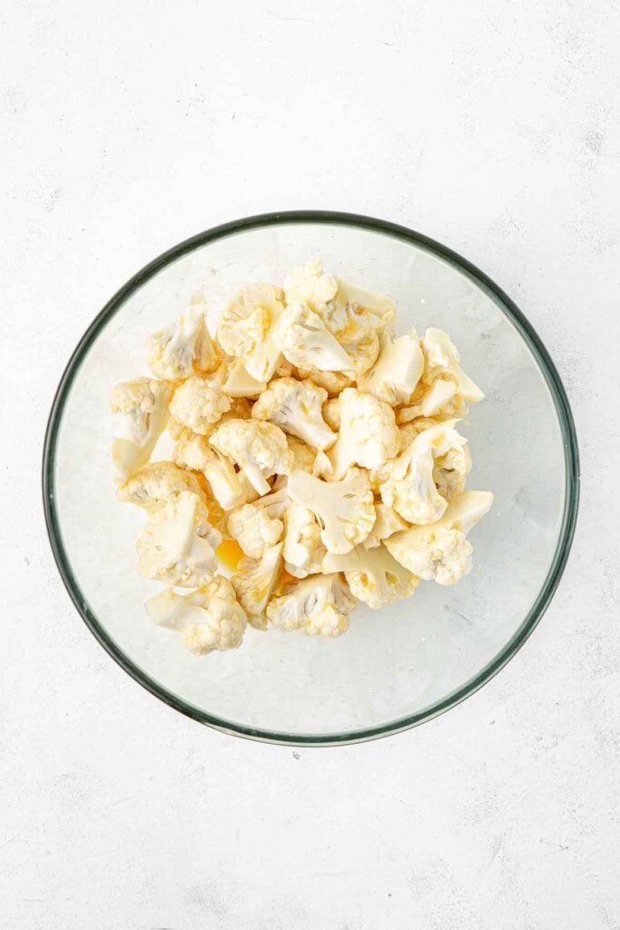 Cauliflower florets tossed in a glass mixing bowl with beaten eggs.