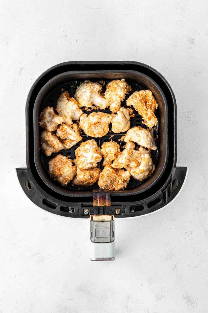 Pieces of cauliflower in a air fryer basket.