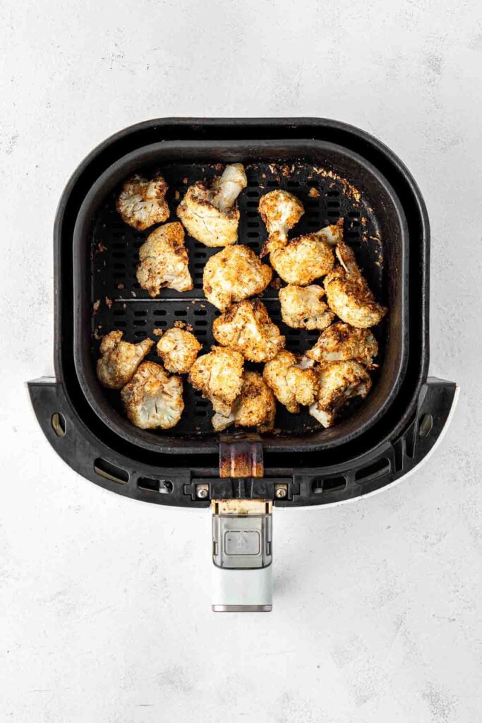 Cooked pieces of cauliflower in the air fryer basket.