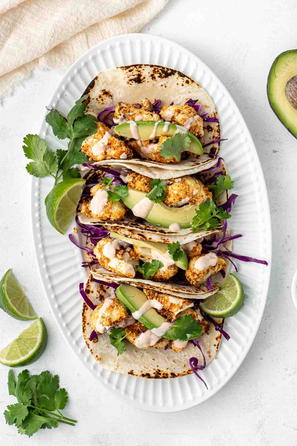 Air fryer cauliflower tacos with red cabbage and avocado on a plate with lime wedges and coriander.  