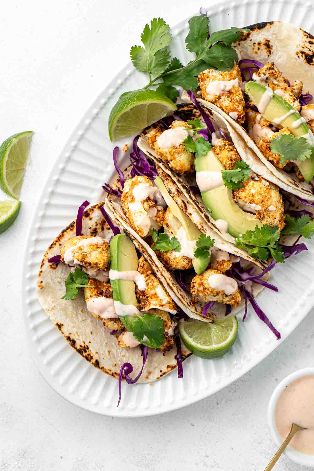 Air fryer cauliflower tacos with red cabbage and avocado on a plate with lime wedges and coriander.  