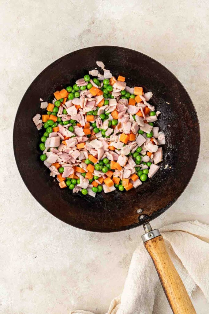 Bacon, peas and carrots in a wok.