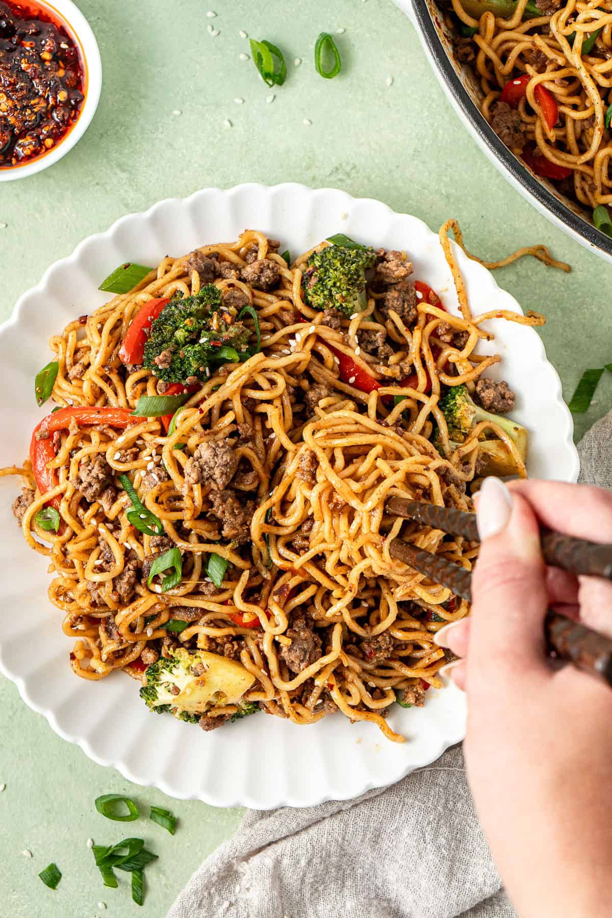 A hand holding chopsticks taking a bite of noodles. 