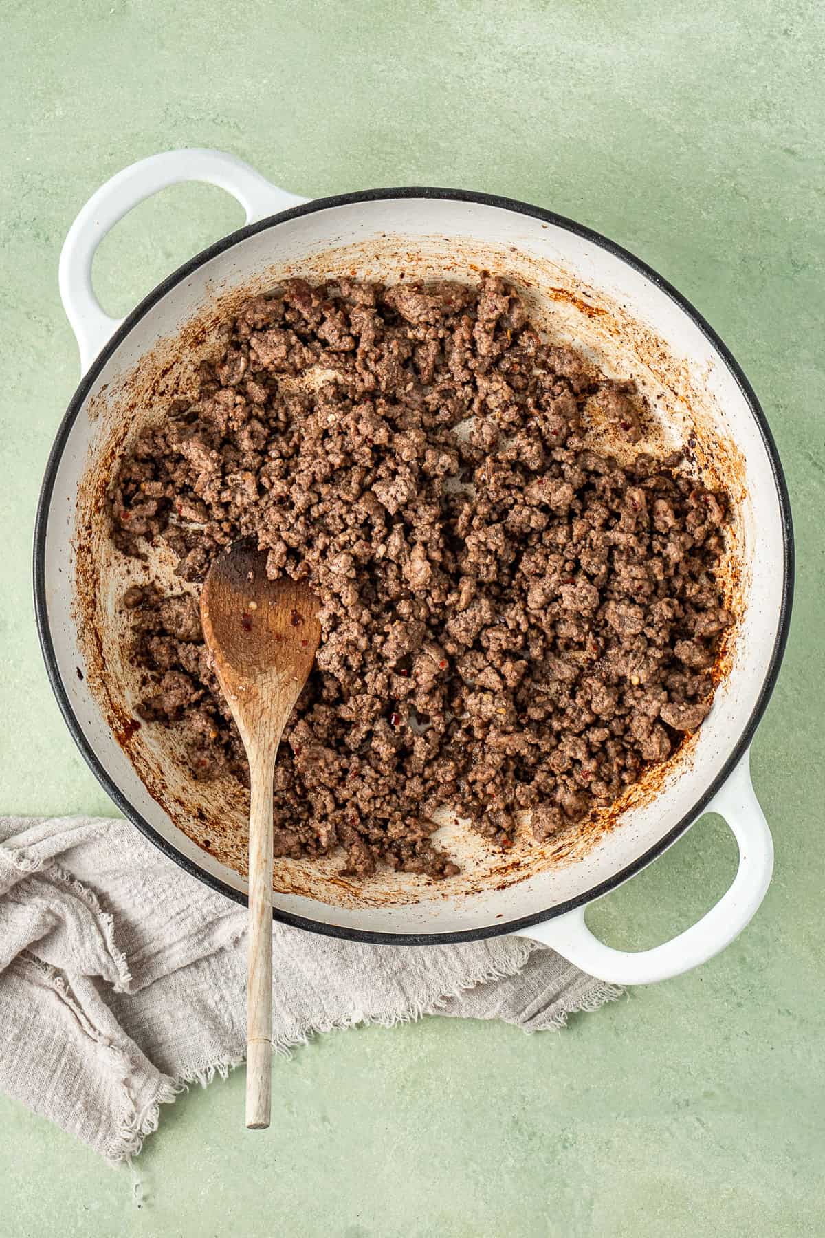The browned beef mince in a pan with a wooden spoon.