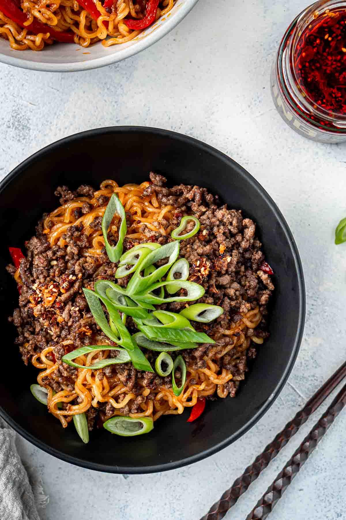 Chilli beef noodles in a black bowl with spring onions.