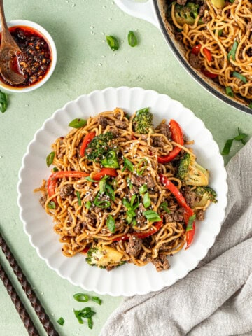 Chilli beef noodles served in a white bowl with chopsticks and chilli oil.