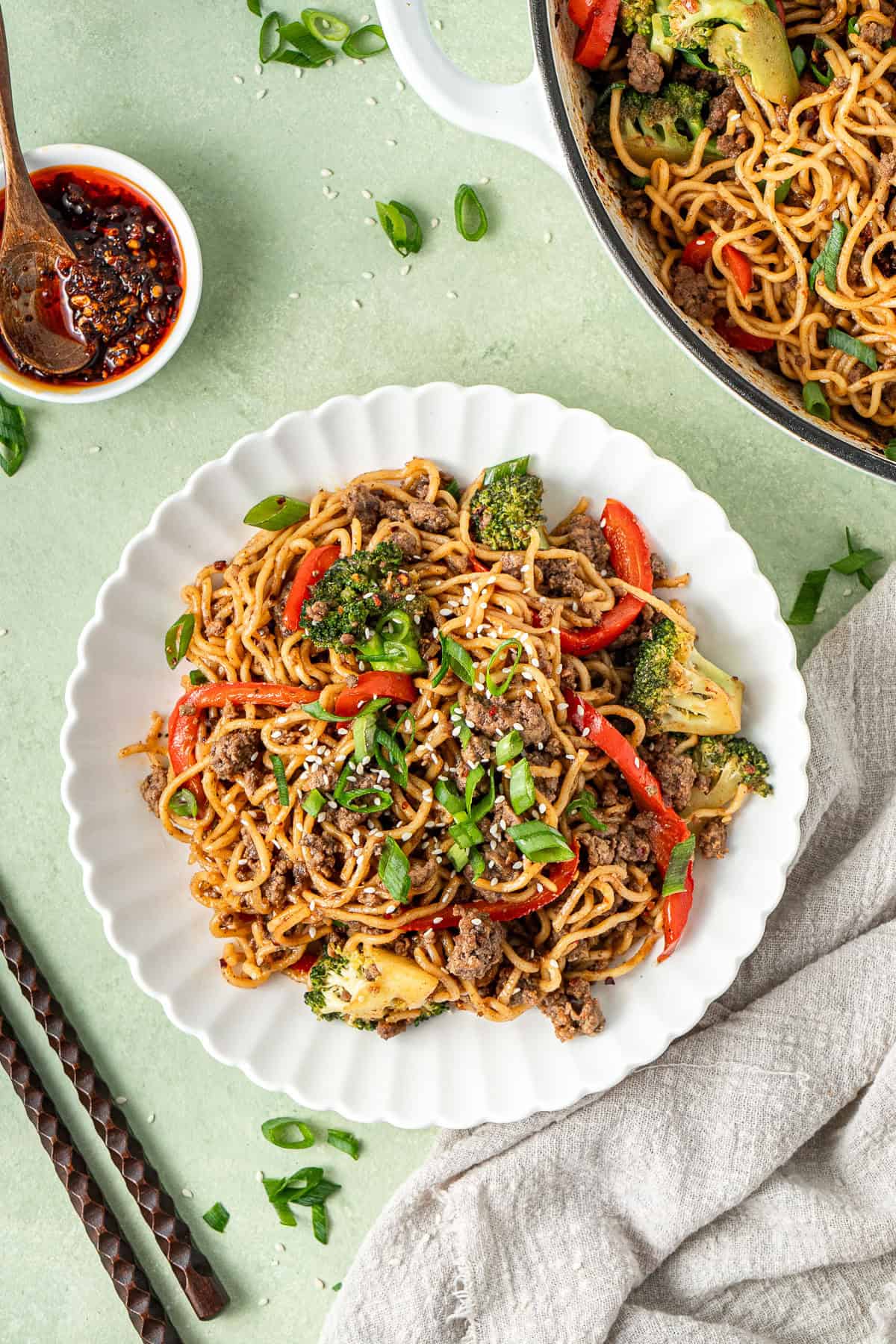 Chilli beef noodles served in a white bowl with chopsticks and chilli oil.
