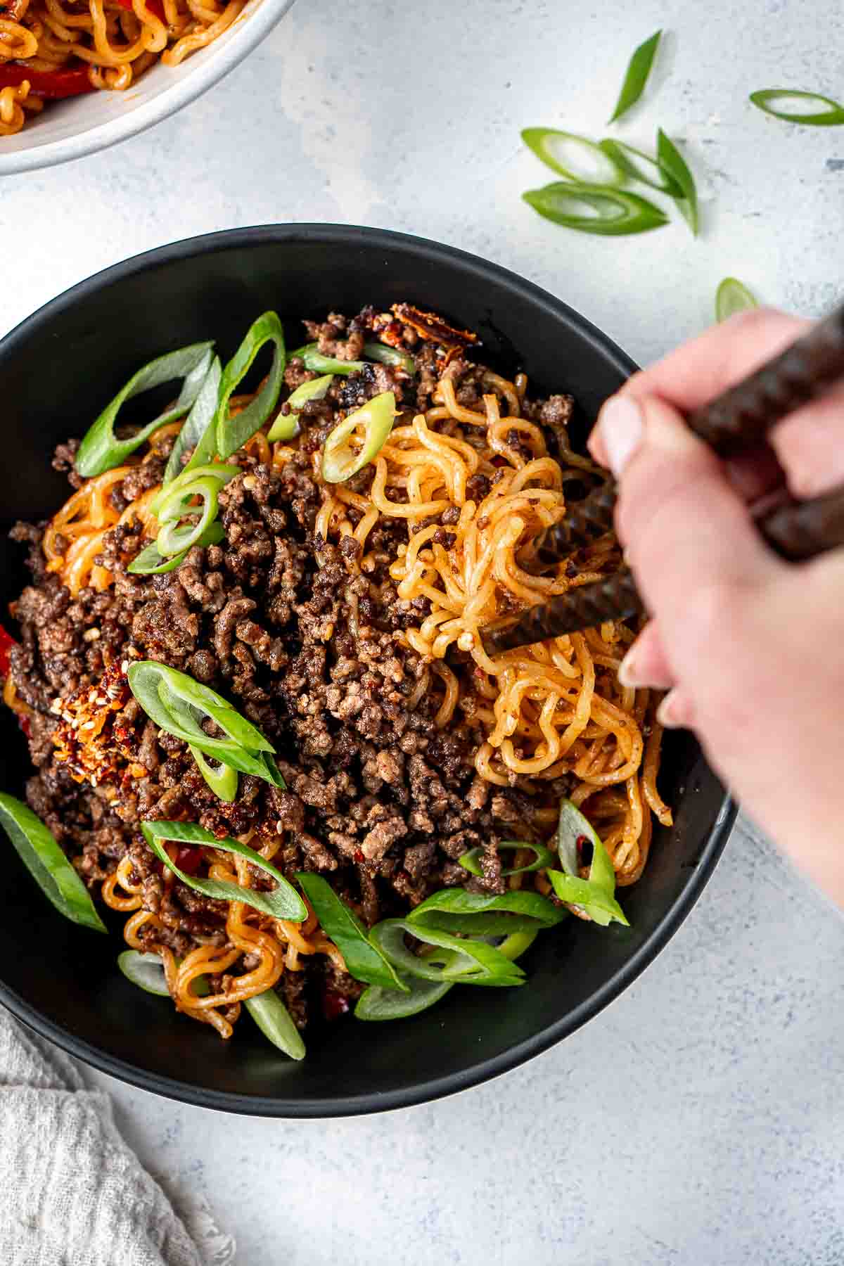 Chopsticks taking a bite of beef noodles with spring onions.