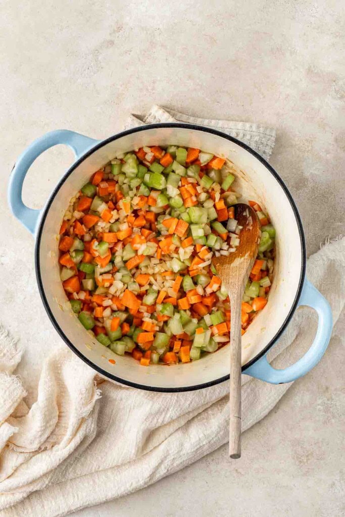 Sautéing the vegetables in the dutch oven with a wooden spoon.