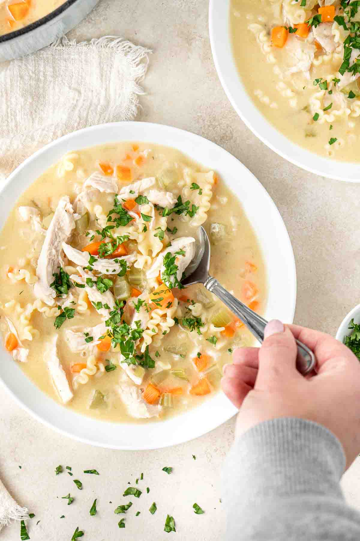 A hand taking a spoon of dairy free creamy chicken soup with parsley. 