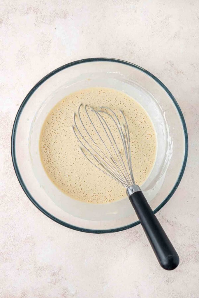 The waffle batter in a glass mixing bowl with a whisk.