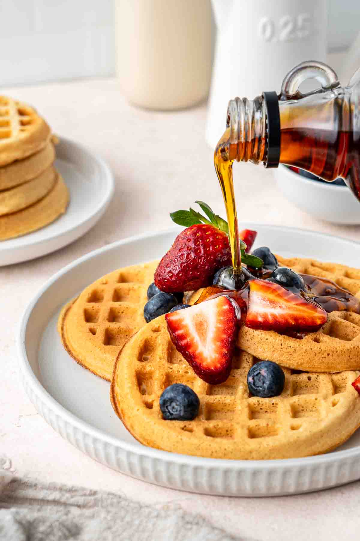 Pouring maple syrup over waffles with fresh berries.