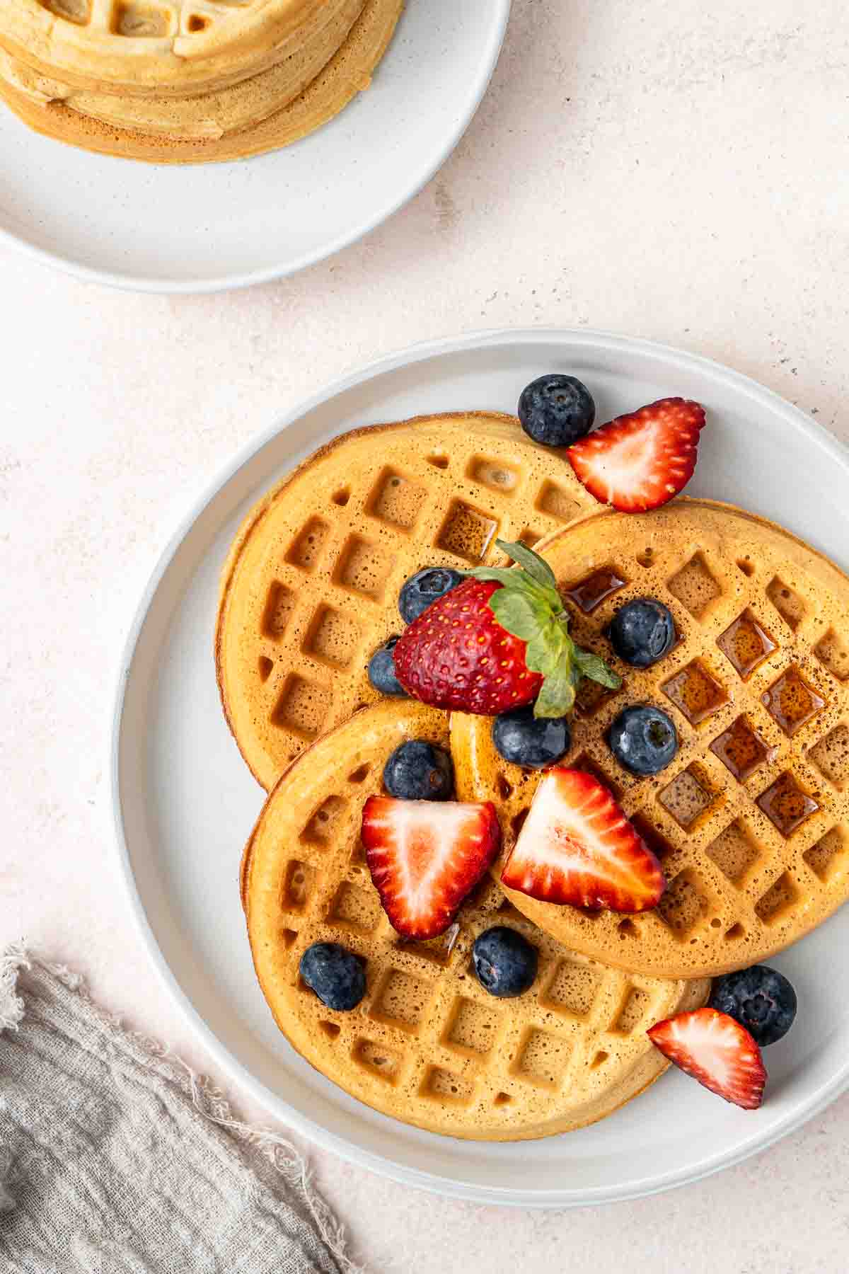 Close up of dairy free waffles with maple syrup and fresh berries on a plate.