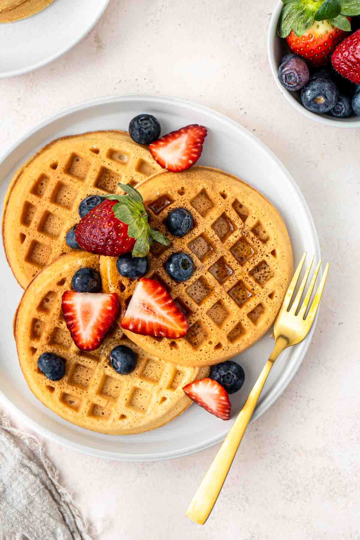 Waffles and berries on a white plate with a fork.