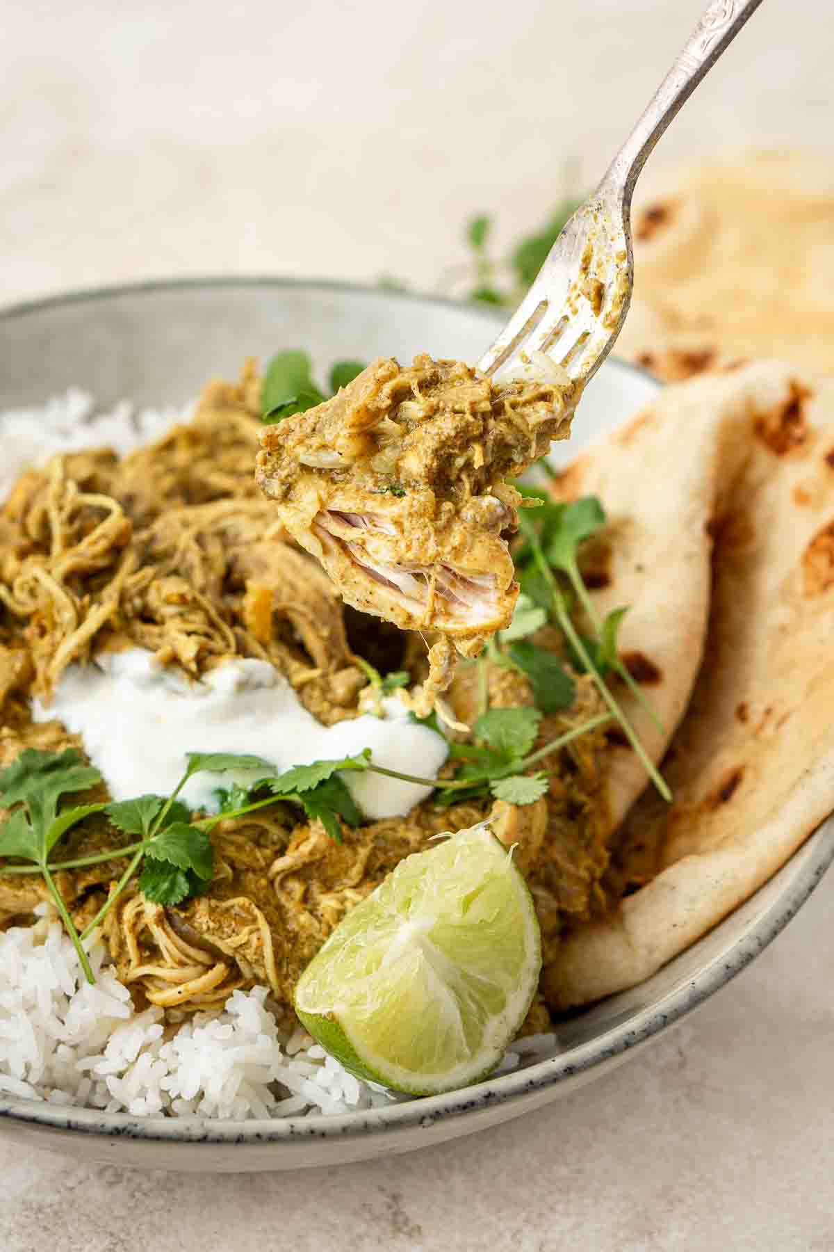 Fork holding up a chunk of tender chicken from a bowl of curry.