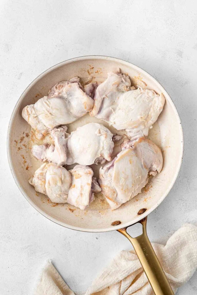 Browning the chicken thighs in a frying pan.