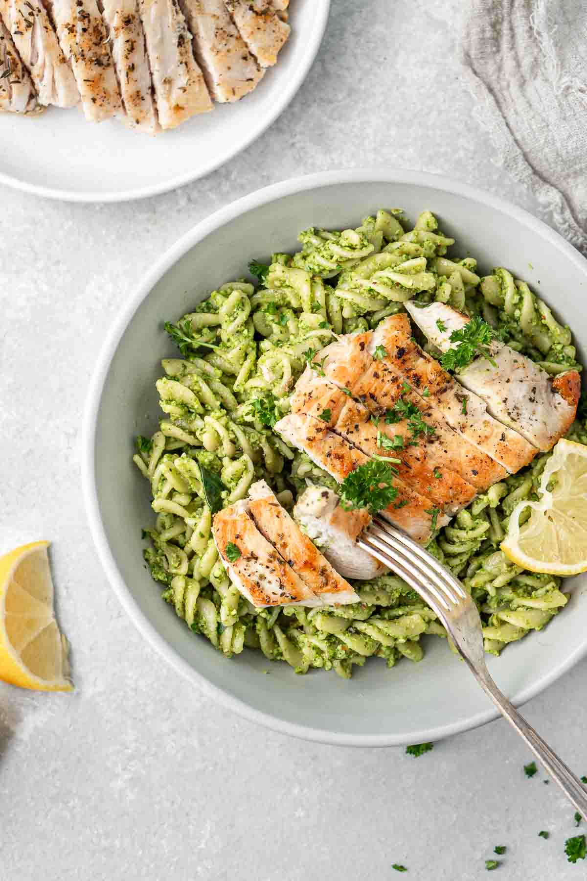 A fork taking a bite of grilled chicken and spinach pesto pasta from a bowl.