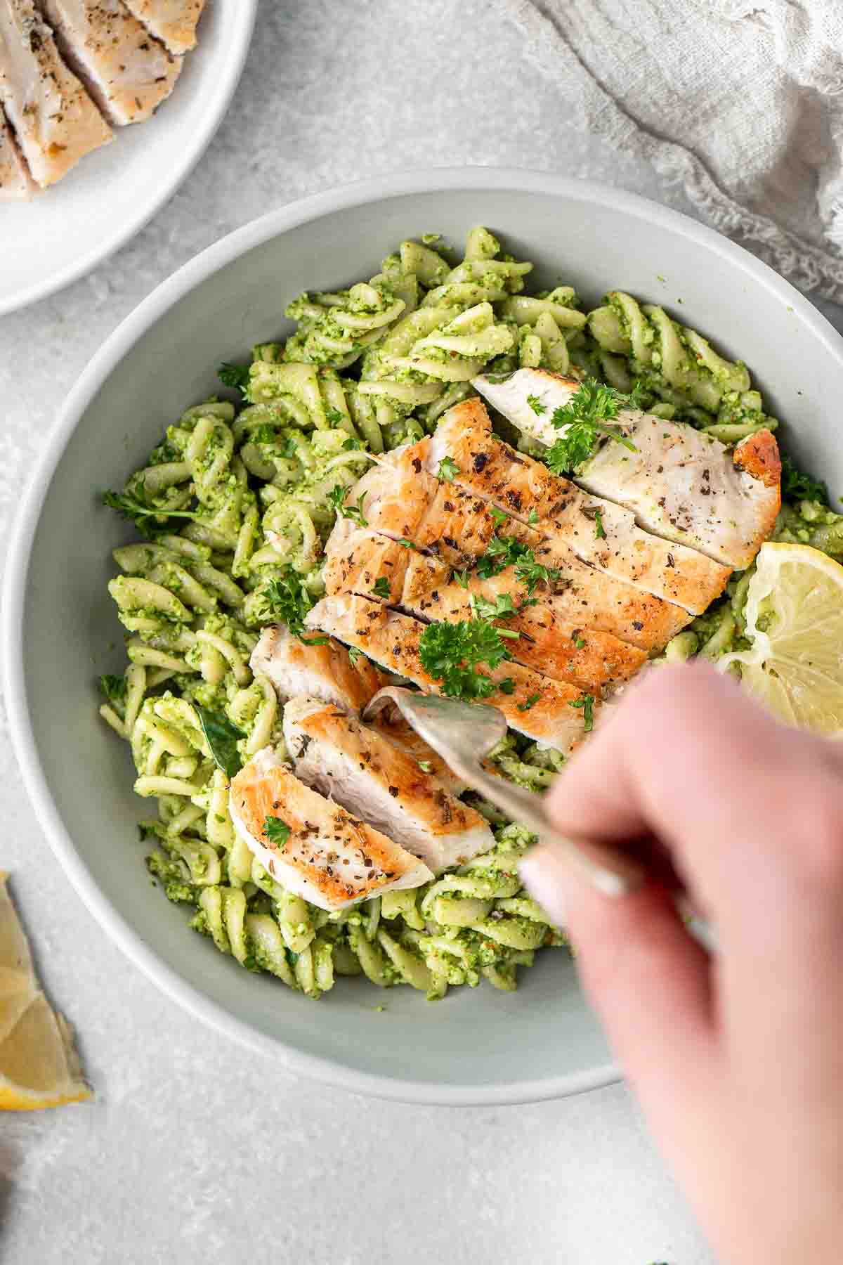 A fork taking a bite of chicken and pesto pasta.