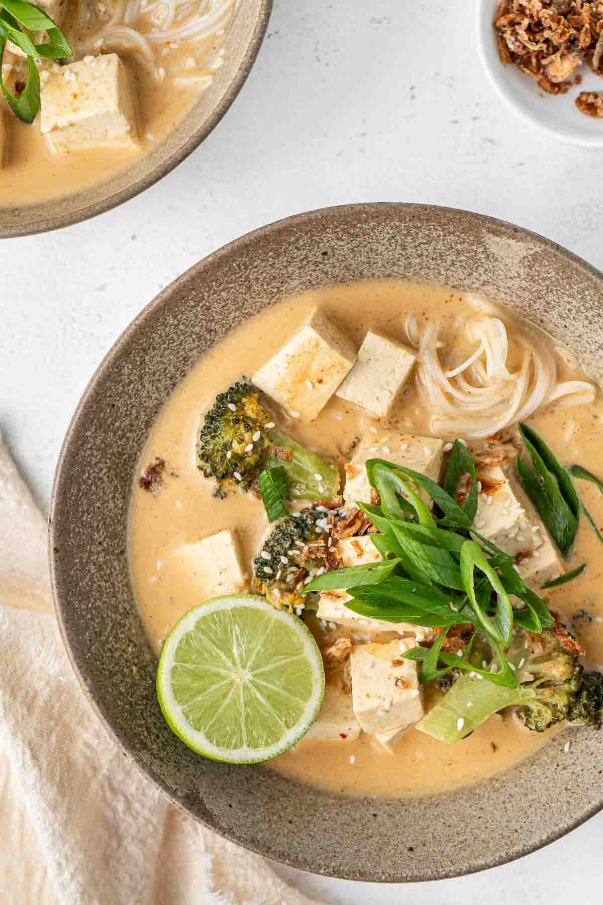 Close up of red curry noodle soup in a bowl with lime and spring onions.