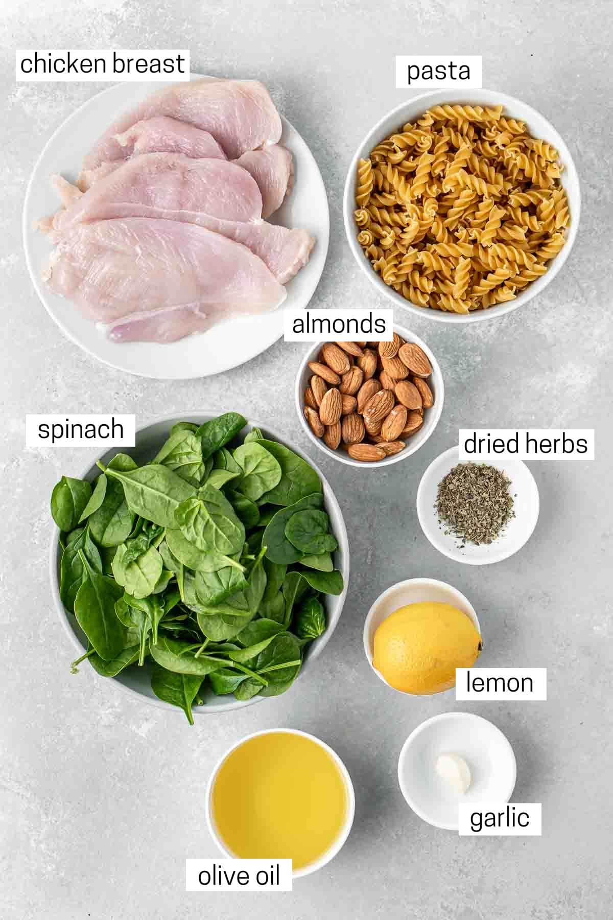 All ingredients needed for spinach pesto pasta with chicken laid out in small bowls.