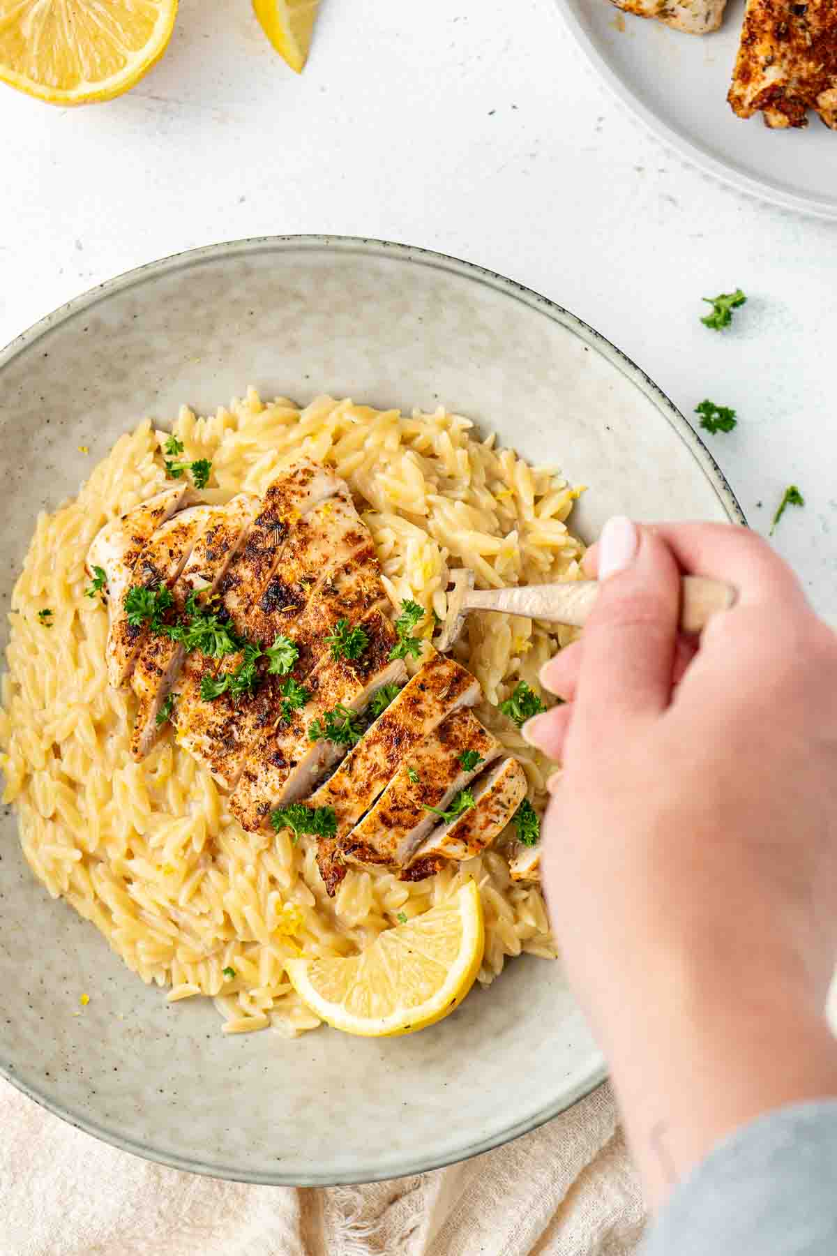 A hand taking a forkful of the creamy lemon risoni with chicken from a bowl.