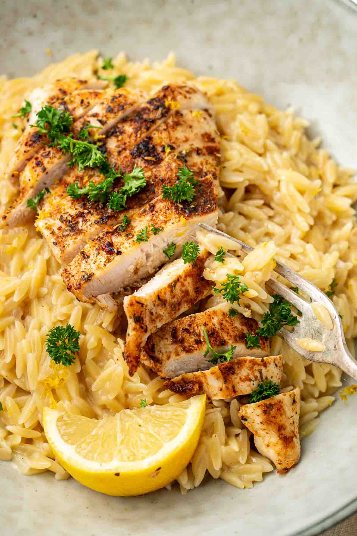 Close up of sliced grilled chicken over creamy lemon risoni.